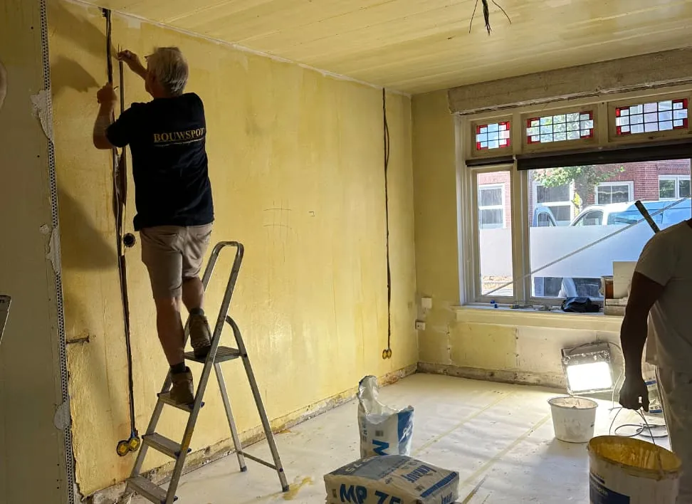 Bouwspot-medewerker werkt vanaf een trapje in een kamer met glas-in-lood ramen