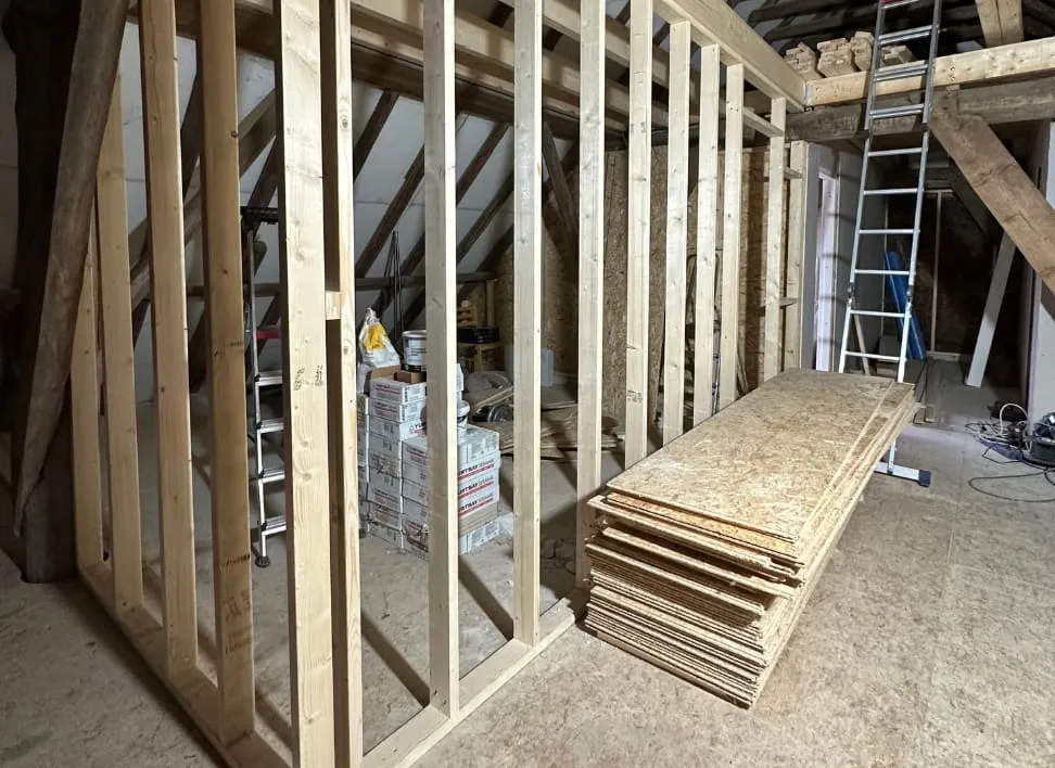Zolder in aanbouw met een nieuw houten wandframe en een stapel OSB-platen