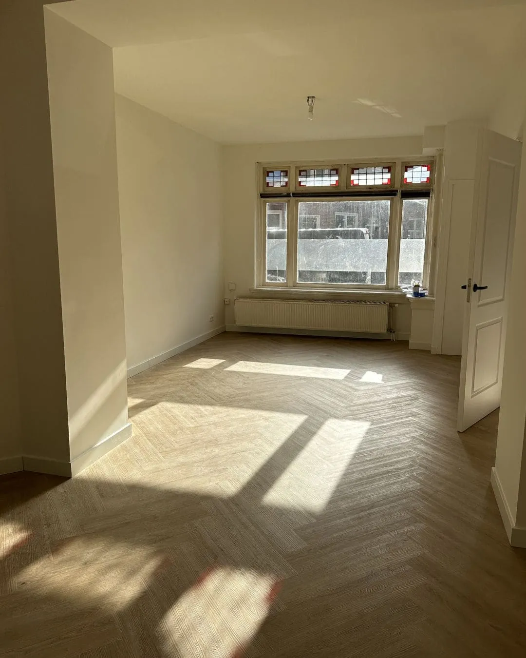 Gerenoveerde woonkamer aan de Moesstraat met visgraatvloer en glas-in-lood bovenlichten
