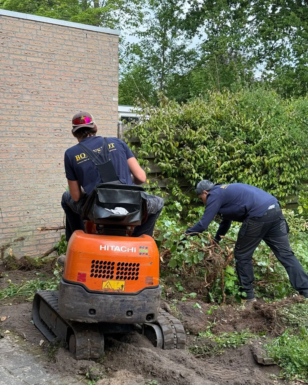 Twee Bouwspot-medewerkers ruimen met een minigraafmachine de tuin leeg voor de renovatie in Paterswolde