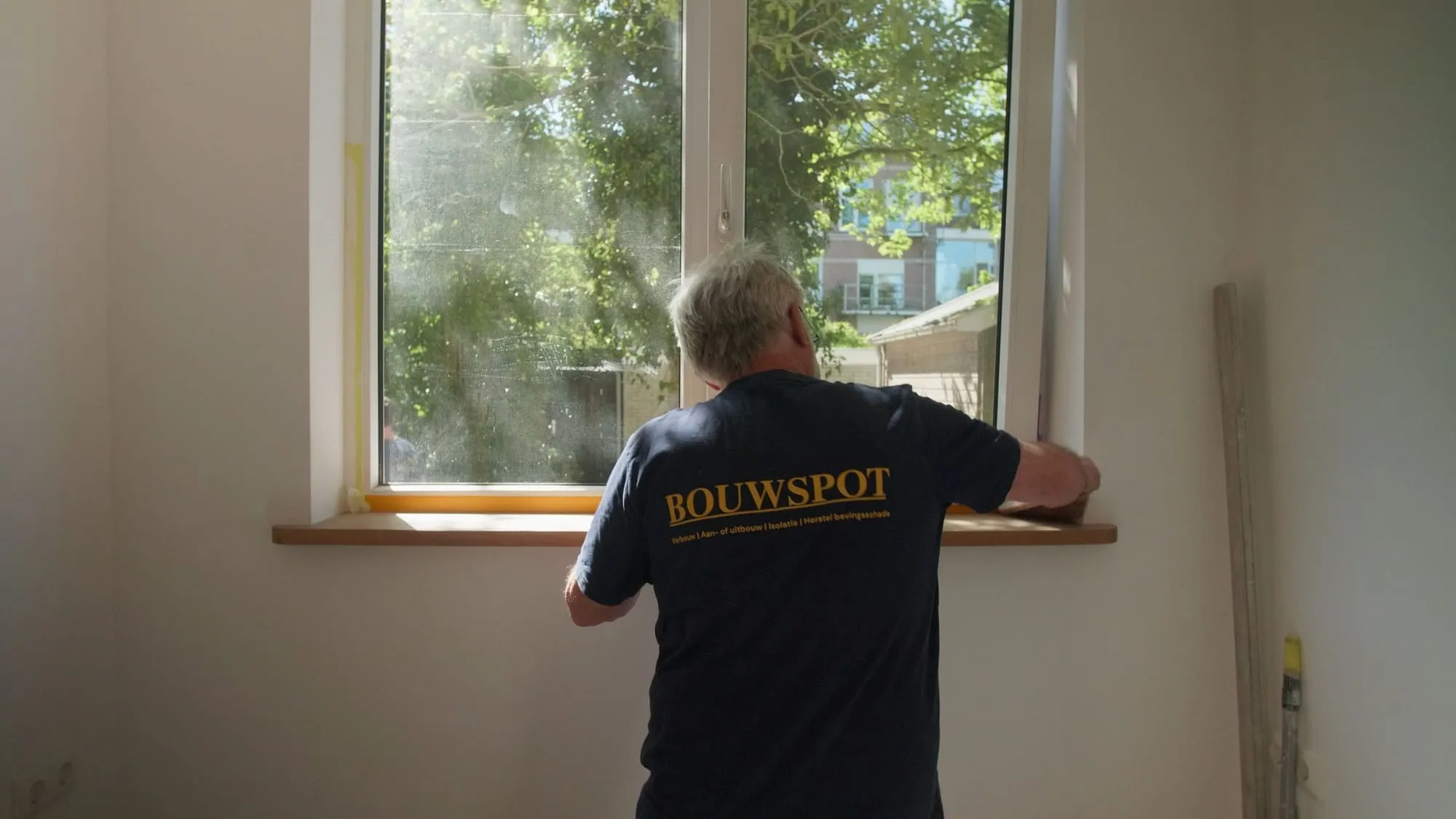 Timmerman van Bouwspot werkt aan een vensterbank bij een raam in een lichte kamer