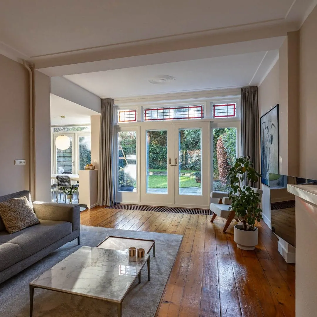 Lichte woonkamer met openslaande tuindeuren, glas-in-loodbovenlichten en een houten vloer